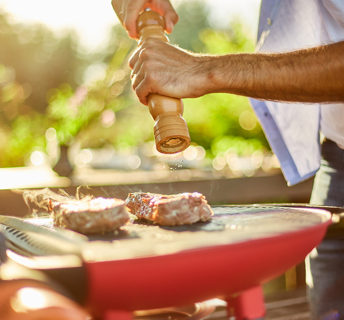 Close up on man's hand seasoning meat on the gas grill on barbecue grill outdoor